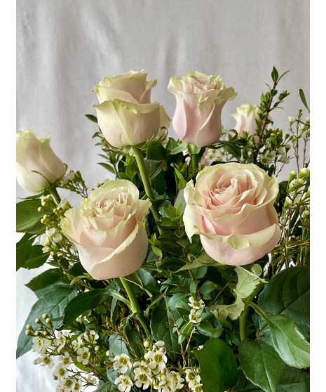 Blushing pink roses are accented with lovely green foliage in a glass vase will make anyone’s heart melt. 