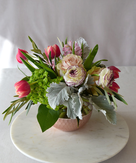 Shades of pink roses, double peony tulips, hyacinths, ranunculus with hydrangea creates a lovely composition in a glass bowl vase with a scalloped light pink metallic finish. 